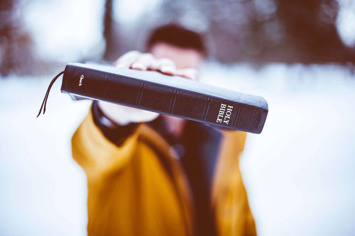 blurry man holding up bible in front of camera white snow background