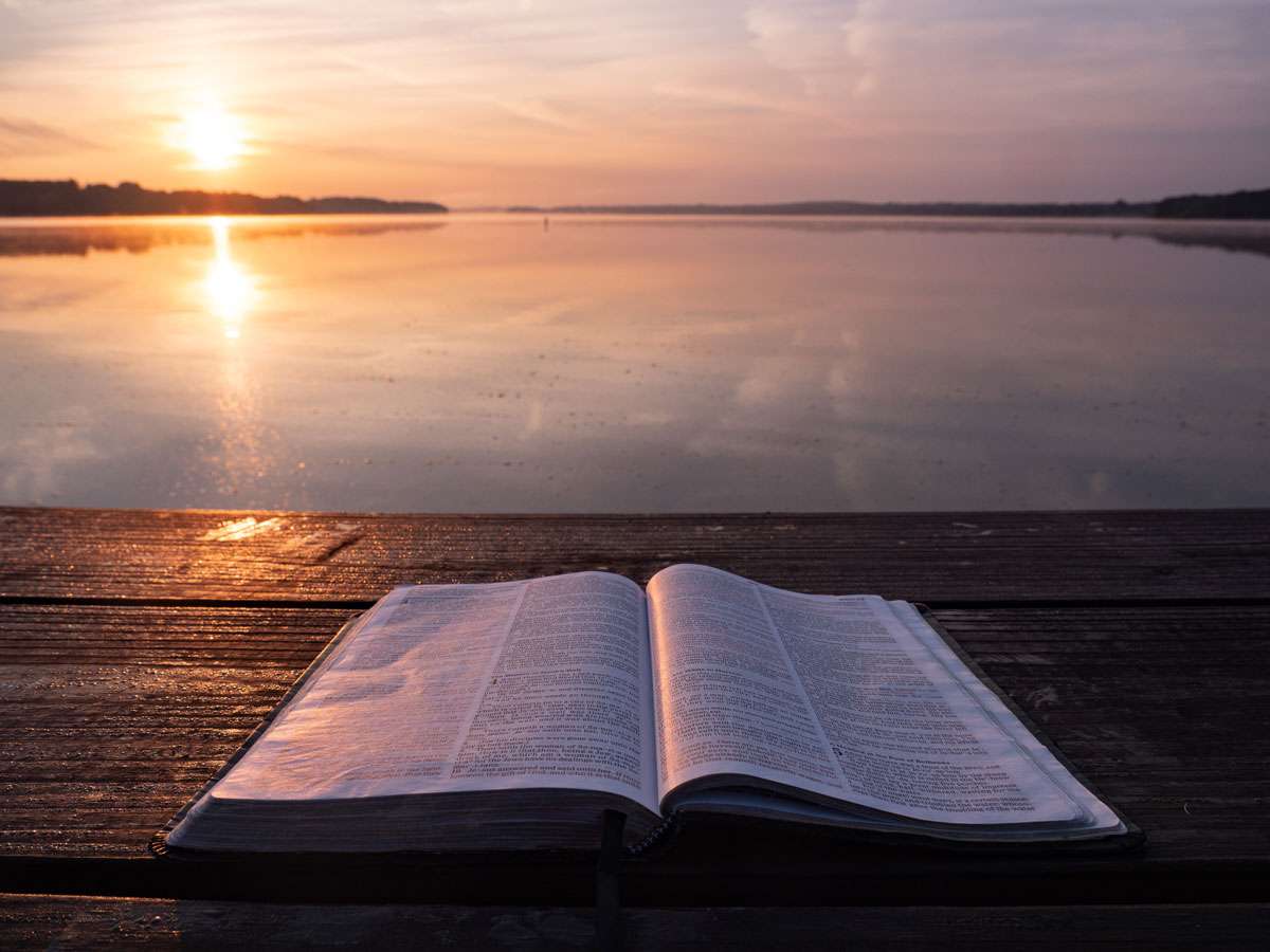 open bible flat on timber picnic bench table with flat ocean behind